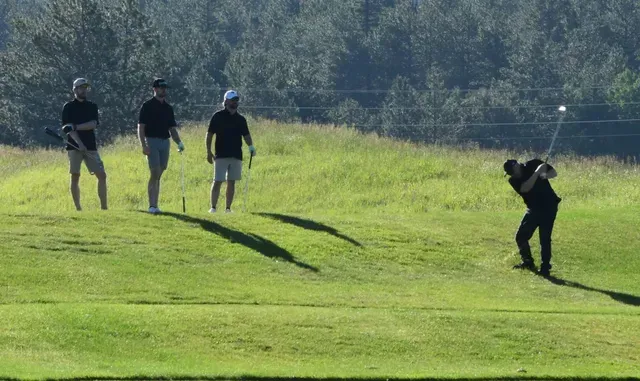 Golfer swings on a green, with three spectators watching. Sunny day on a golf course.