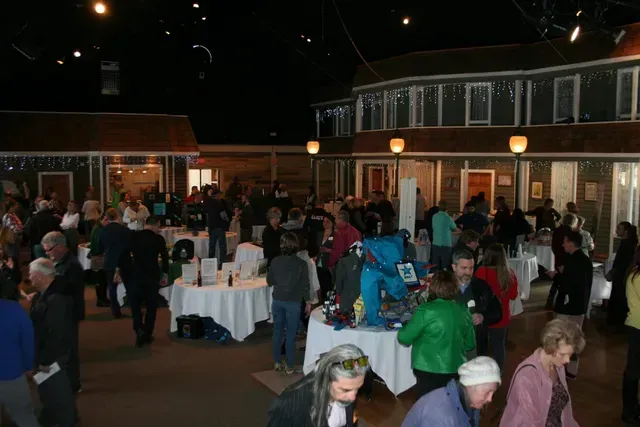 People gathered at an event in a building with shop-like structures, tables, and decorations.