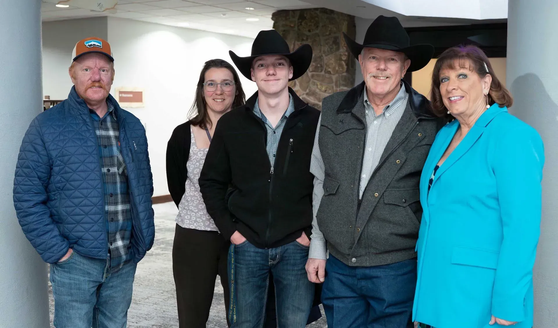 A group of five people posing for a photo in an indoor setting. Cowboy hats and jackets are visible.