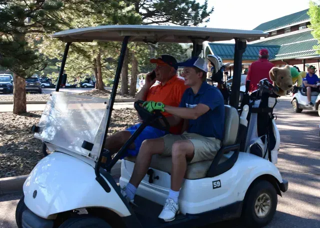 Two men in a white golf cart. One talks on the phone, the other drives.
