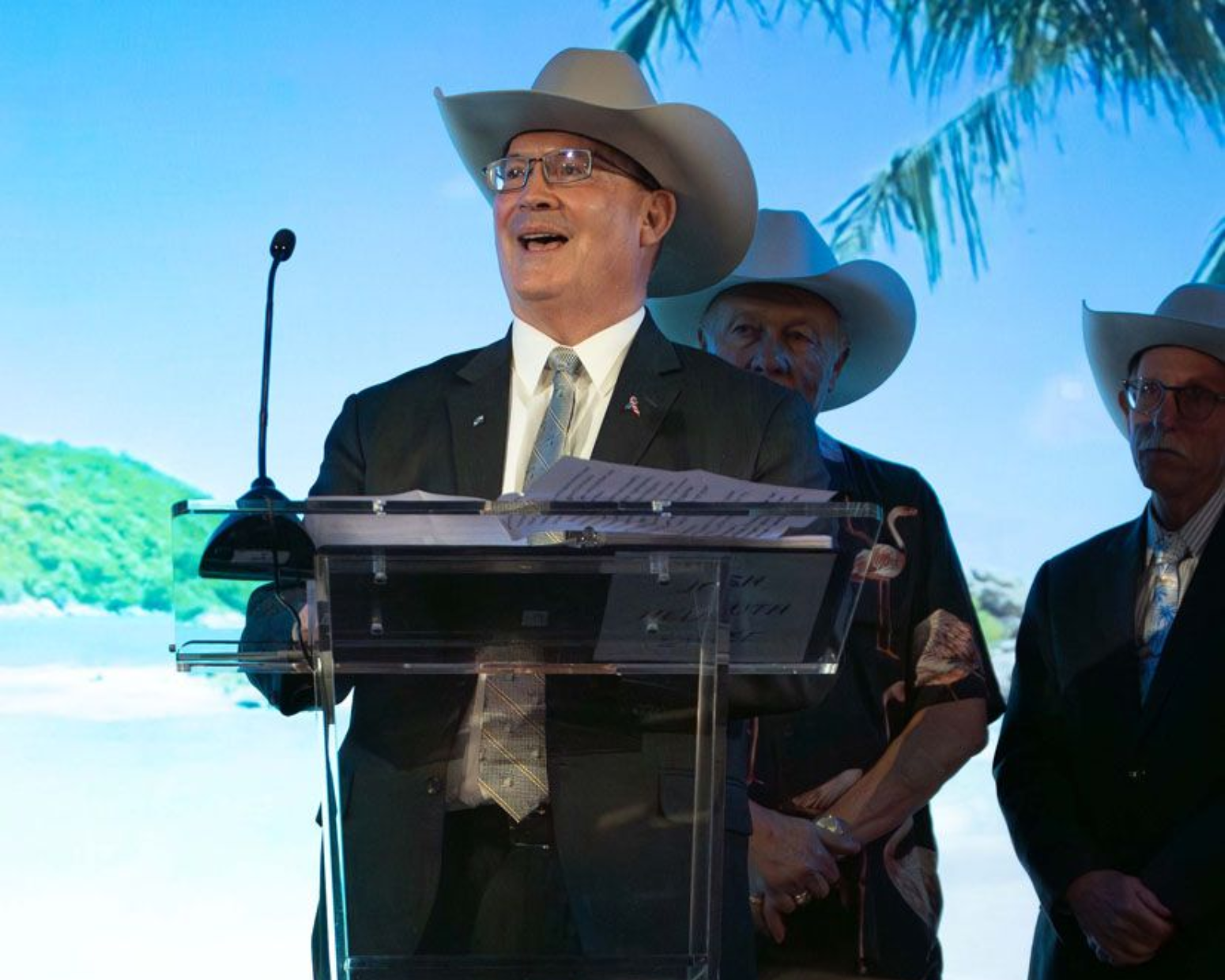 Two men in cowboy hats holding an award on stage, one wearing a dark jacket and the other a brown jacket.