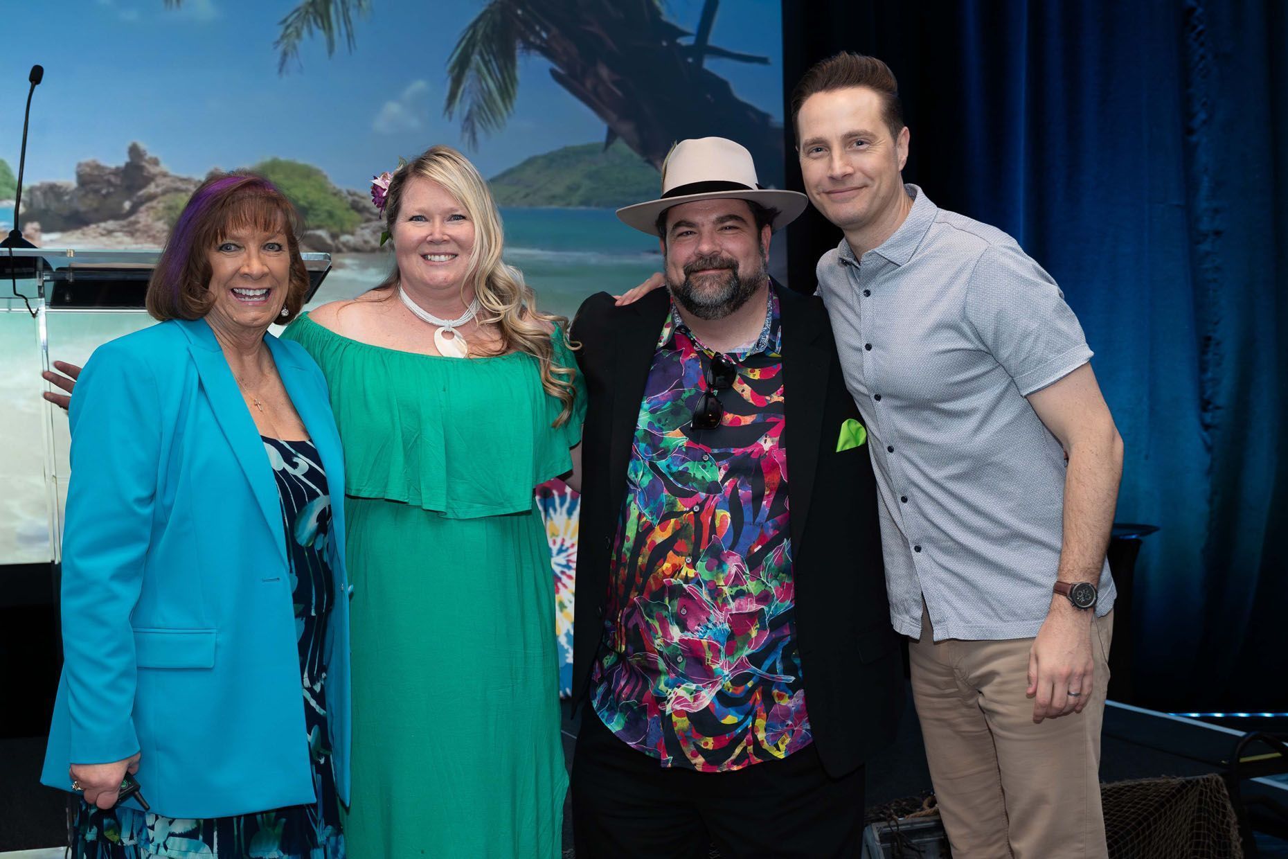 Four people in tropical attire pose together. Backdrop with beach scene.