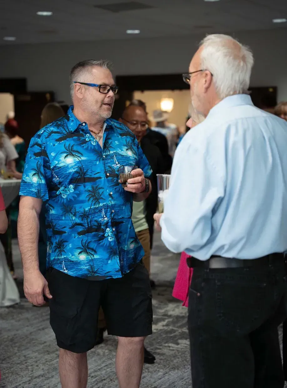 Man in Hawaiian shirt conversing with another man at an event.