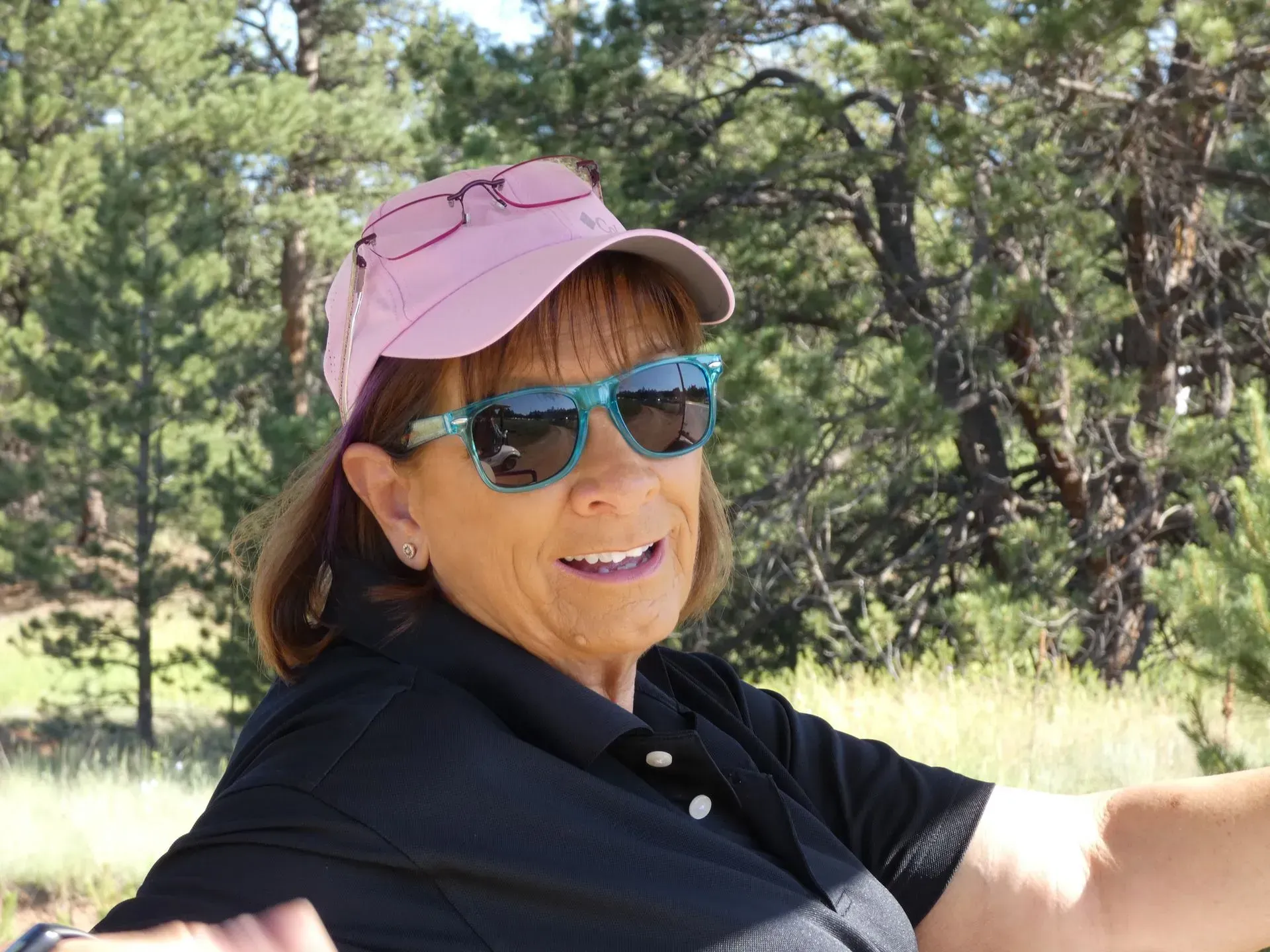 Woman in sunglasses and pink hat smiles outdoors.