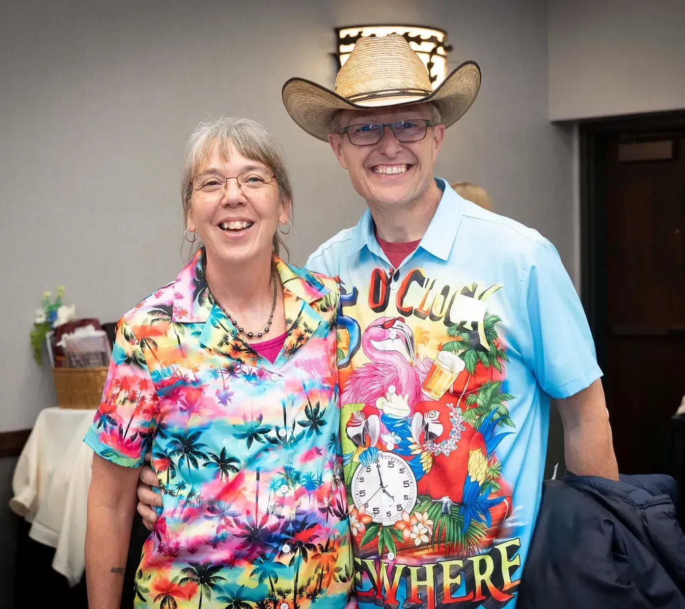 Two smiling people in tropical shirts, man in cowboy hat.