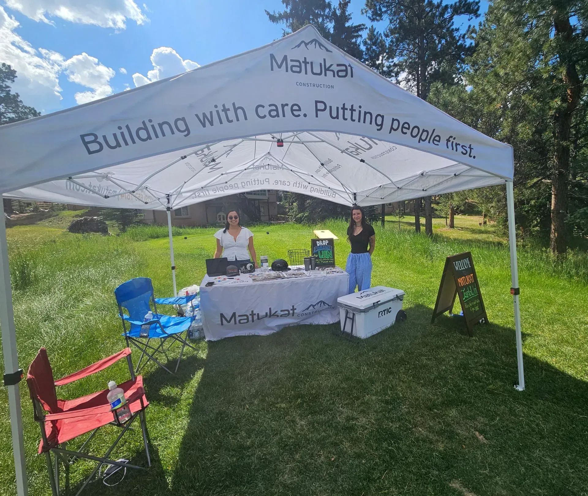Two women at a Matukai booth in a grassy outdoor setting. Booth has a white canopy.