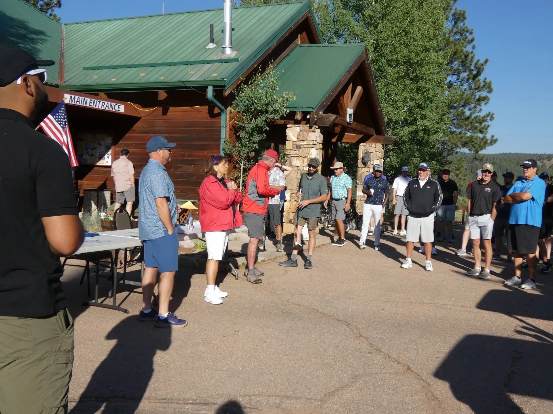 People gathered outside a log cabin with a green roof, possibly for an event.