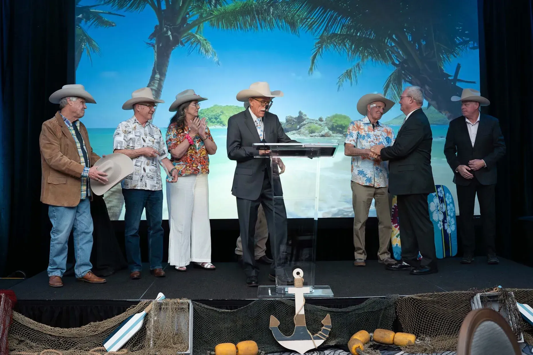 Group of people on stage, some in cowboy hats, receiving an award with a beach backdrop.