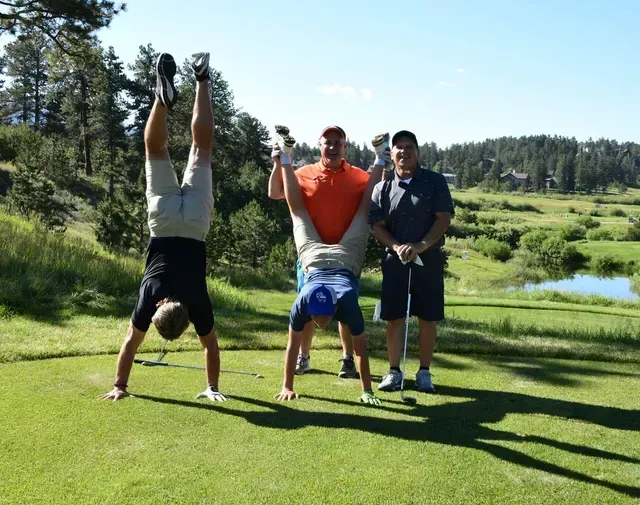 Three men on a golf course, two doing handstands while the third watches. Sunny day.