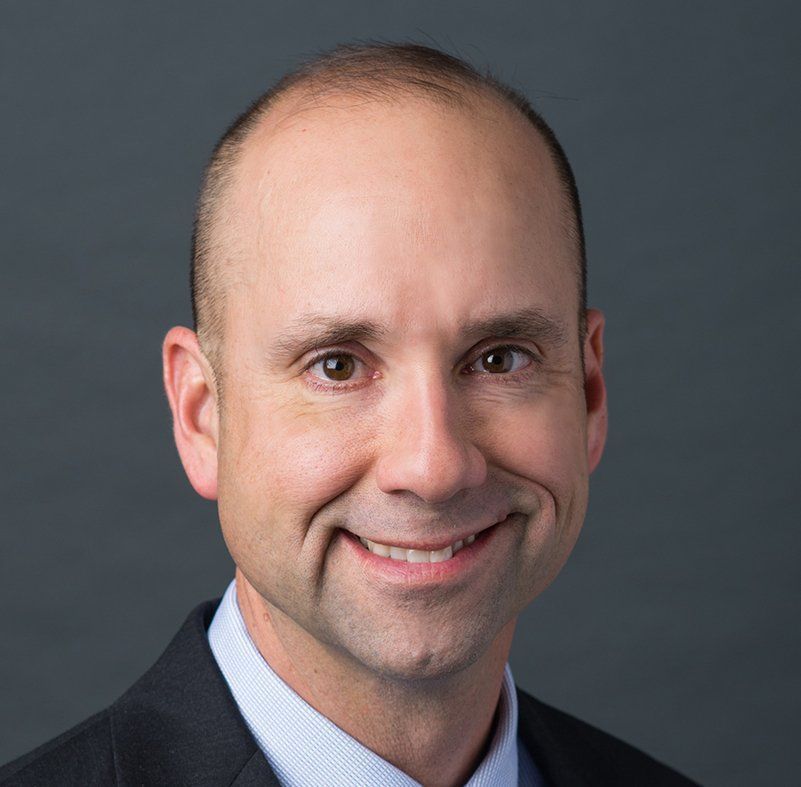 Man with short hair, wearing a suit, smiling.