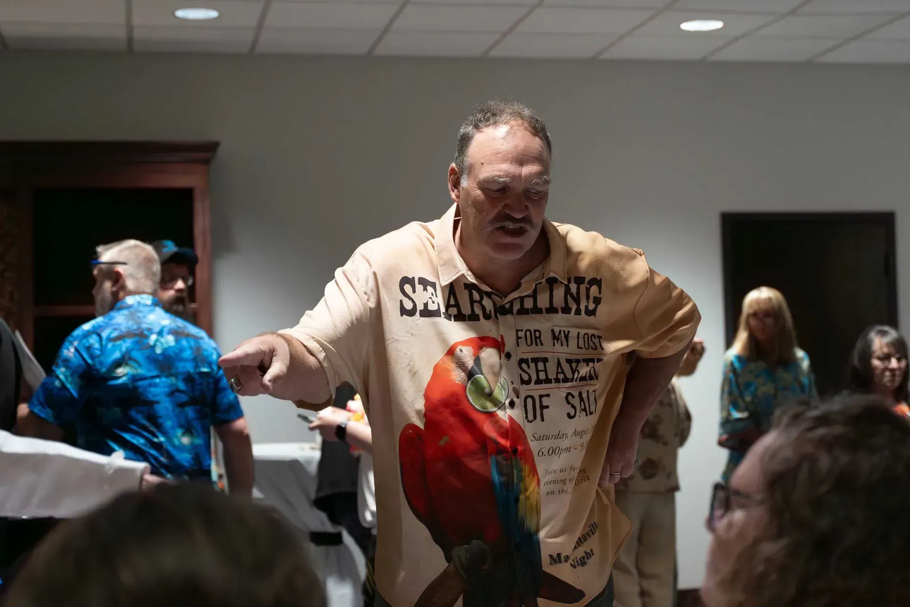 Man in parrot shirt pointing; indoors, group of people.