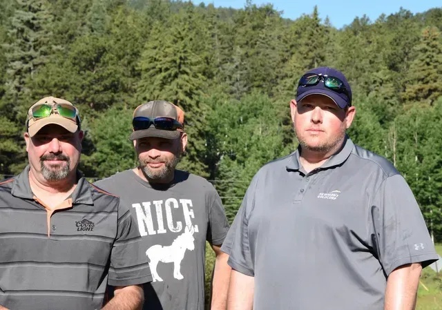 Three men pose outdoors with trees in the background.