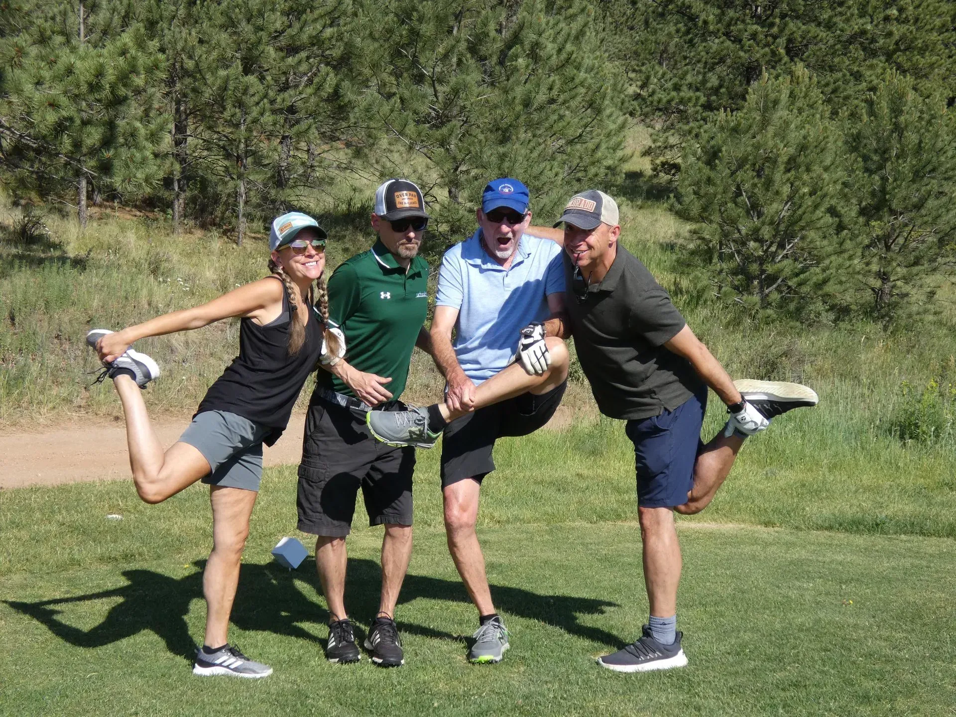 Four people in athletic wear stretching on a golf course, sunny day.