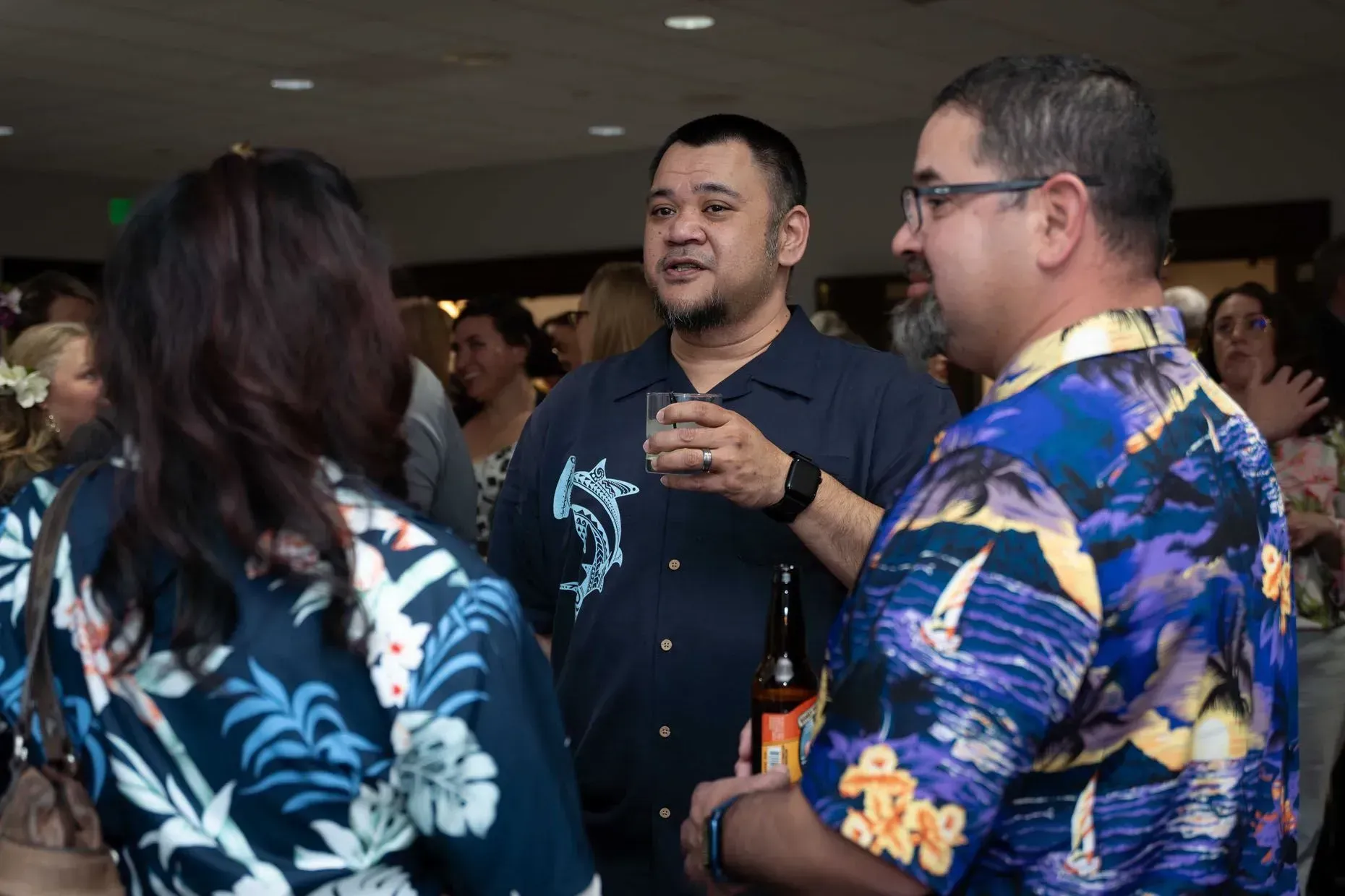 Three people in Hawaiian shirts talking at a social gathering.