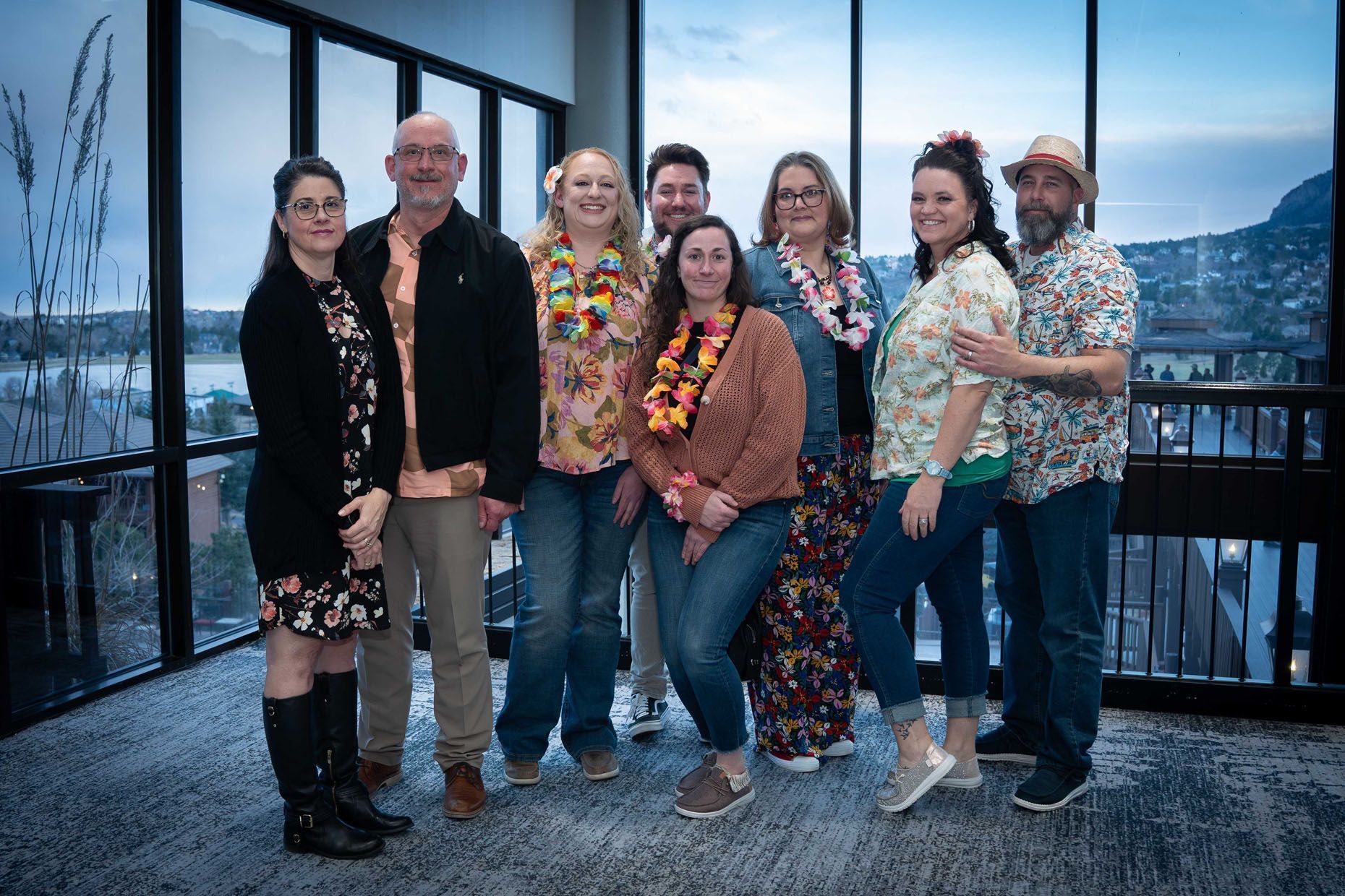 Group of people in Hawaiian attire, smiling, posing for a photo indoors with a scenic background.