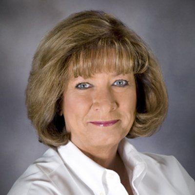 Woman with short, layered blonde hair, wearing a white collared shirt, smiling.