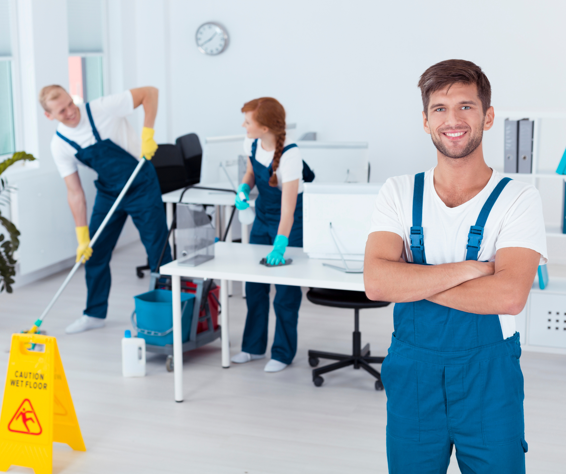 A smiling person in blue overalls poses, while two others clean an office; one mops, the other wipes a desk.