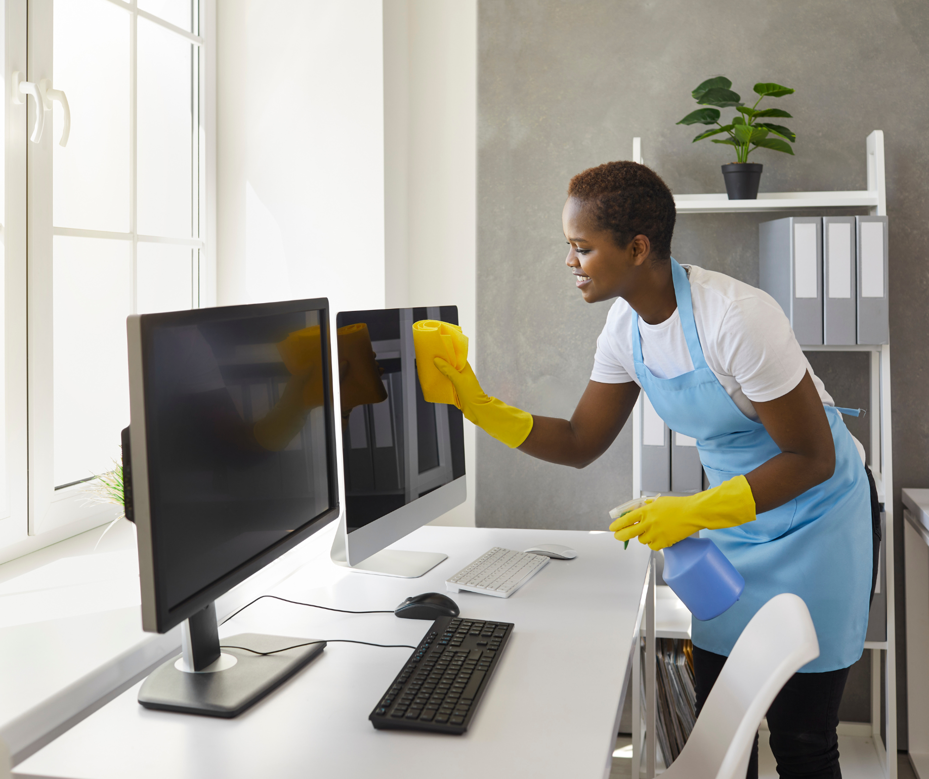 Person wearing gloves and apron cleaning computer screens in an office.