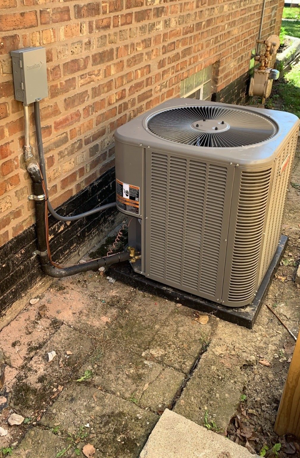 An air conditioner is sitting on the side of a brick building.