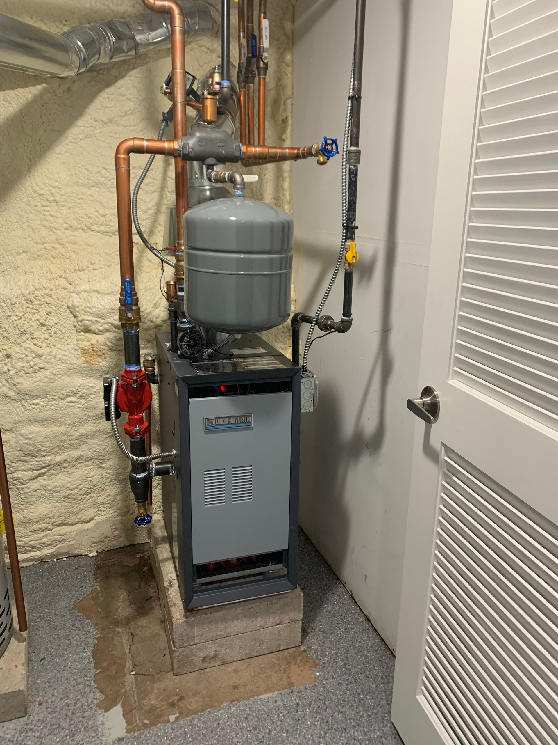 A boiler is sitting in a basement next to a door.
