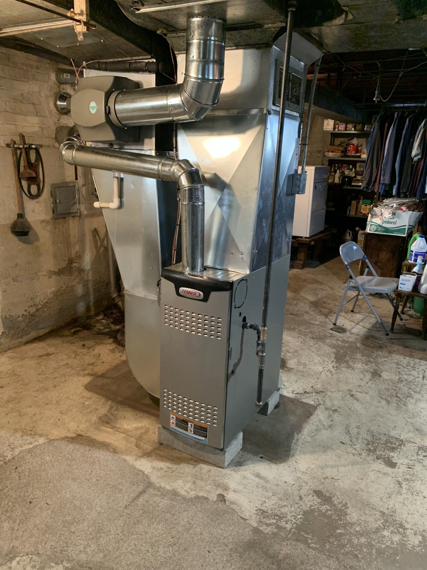 A large heater is sitting in a basement next to a chair.