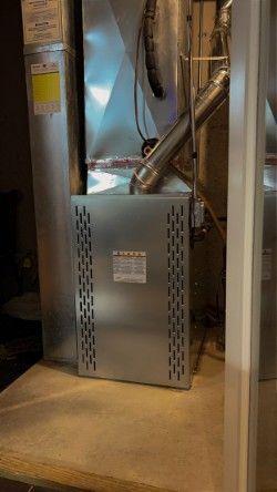 A silver air conditioner is sitting on top of a wooden floor in a basement.