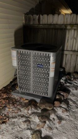 An air conditioner is sitting in the snow outside of a house.
