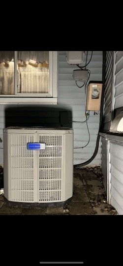An air conditioner is sitting outside of a house next to a window.