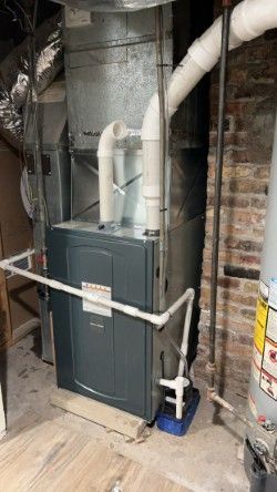 A furnace is sitting in a basement next to a brick wall.