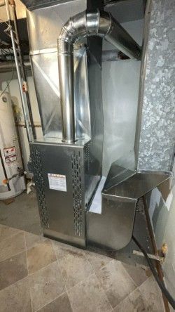 A stainless steel air conditioner is sitting in a basement next to a water heater.