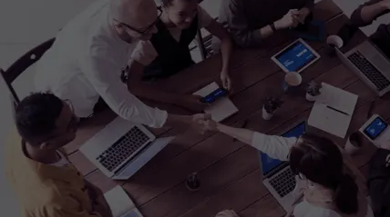 A group of people are shaking hands at a table with laptops.