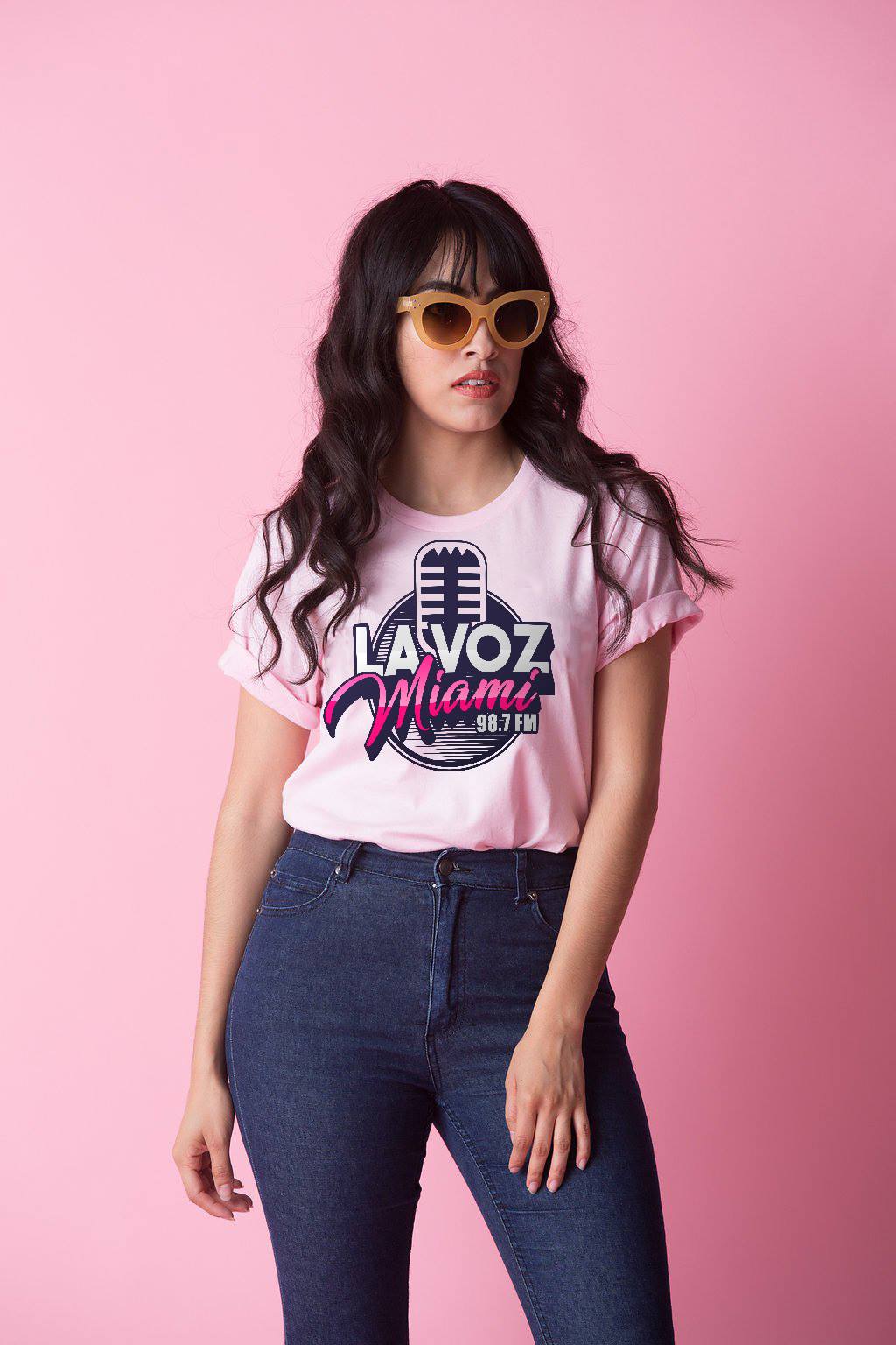 a woman wearing sunglasses and a pink t-shirt is standing in front of a pink background .