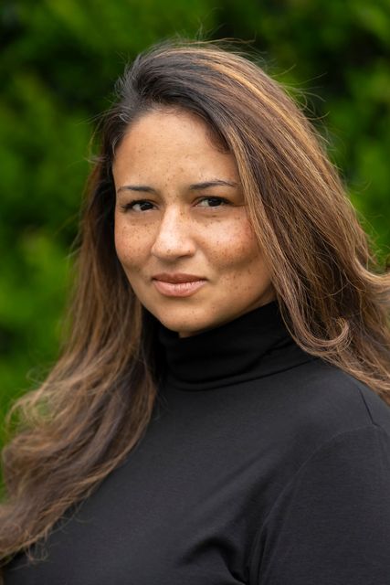 A woman with long hair is wearing a black turtleneck and looking at the camera.