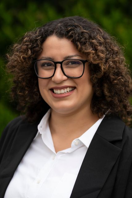 A woman wearing glasses and a black jacket is smiling for the camera.