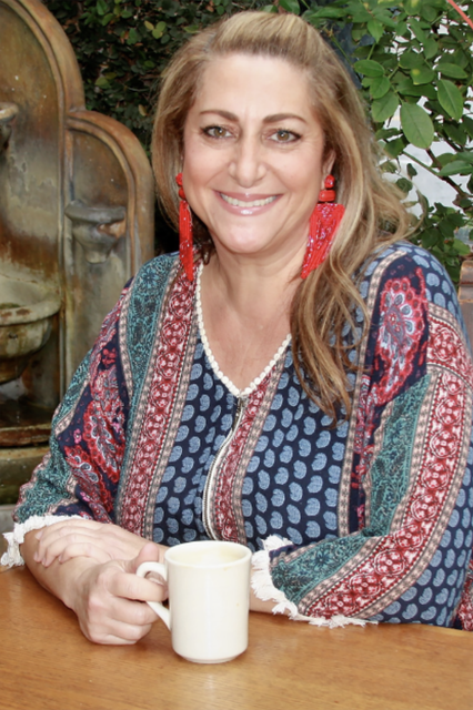 A woman is sitting at a table holding a cup of coffee.