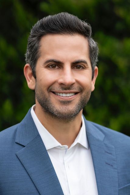 A man in a blue suit and white shirt is smiling for the camera.