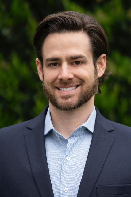 A man with a beard is wearing a suit and smiling for the camera.