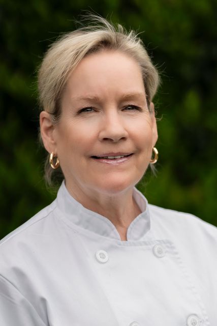 A woman in a chef 's coat is smiling for the camera.
