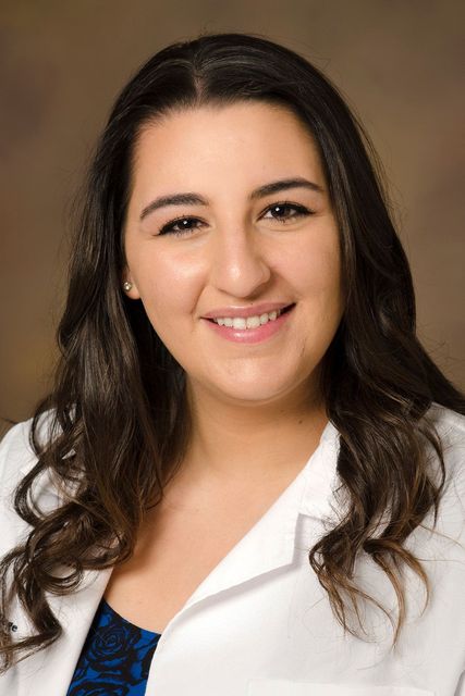 A woman in a white lab coat is smiling for the camera.