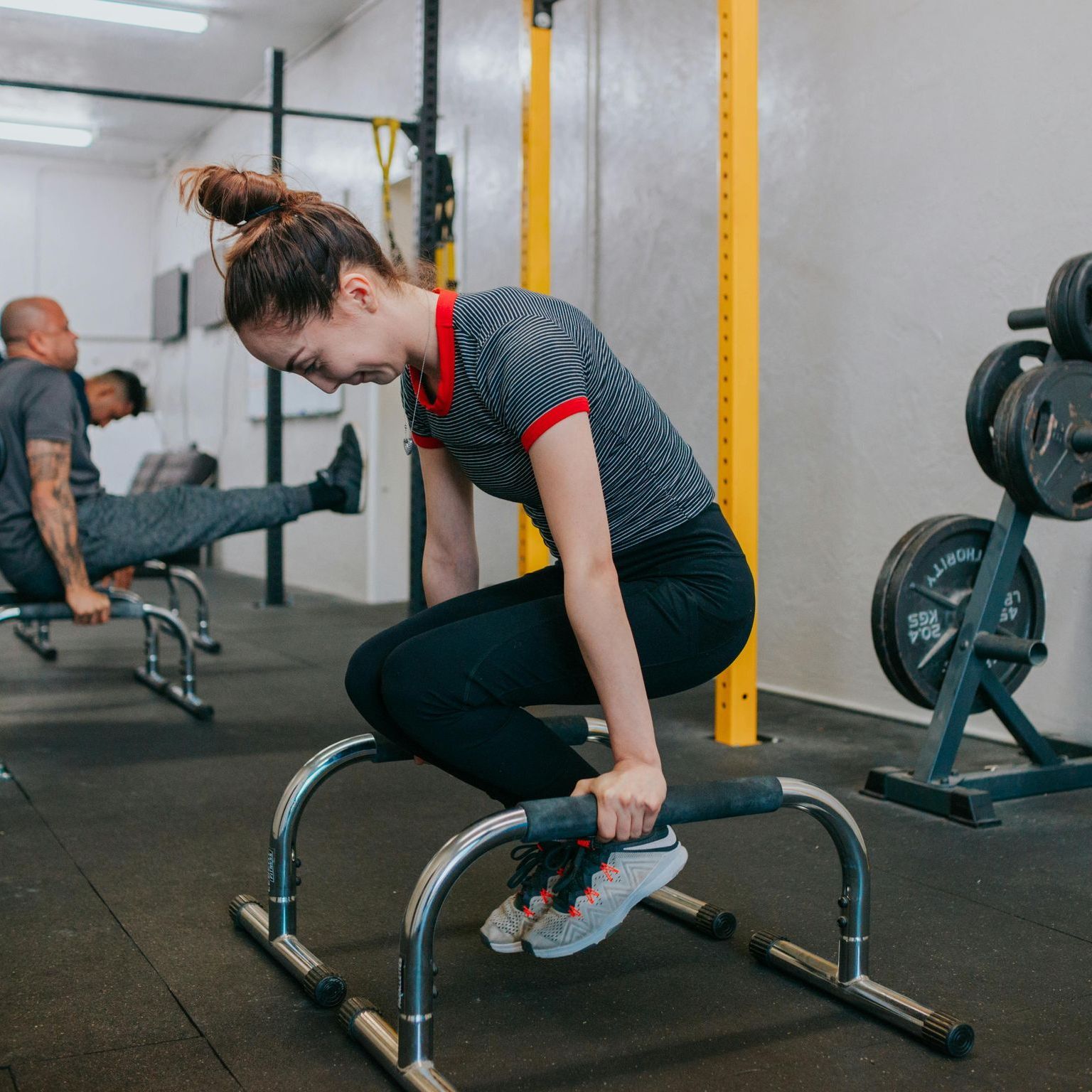 A woman is squatting on parallel bars in a gym