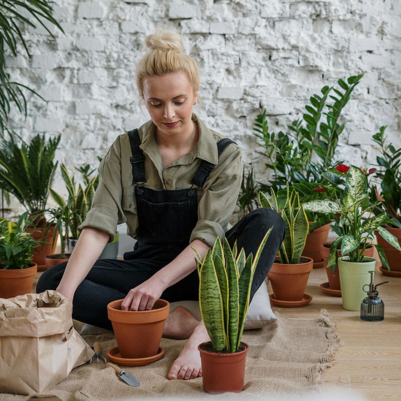 A woman is sitting on the floor surrounded by potted plants