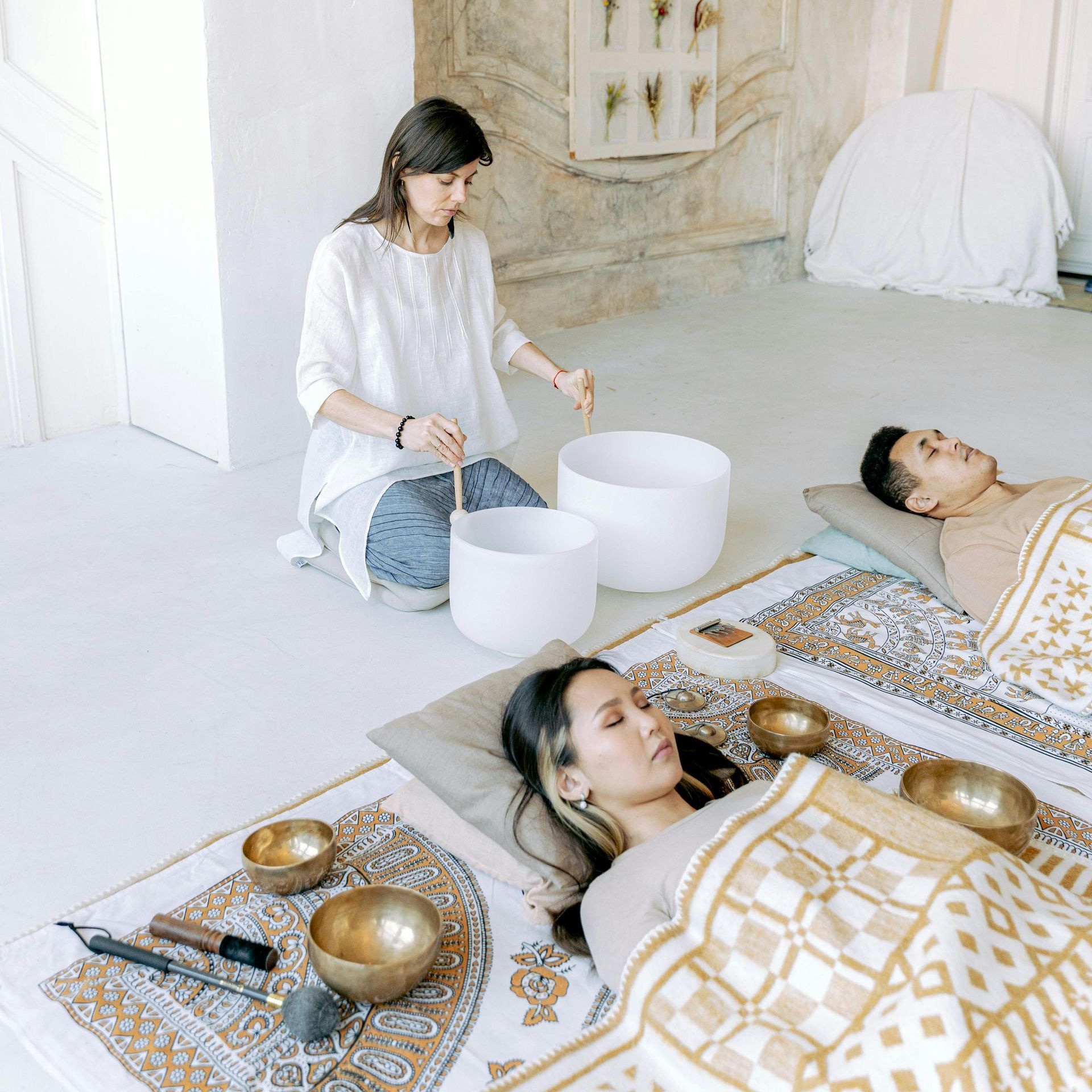 A woman is playing singing bowls to a man and a woman laying in bed.