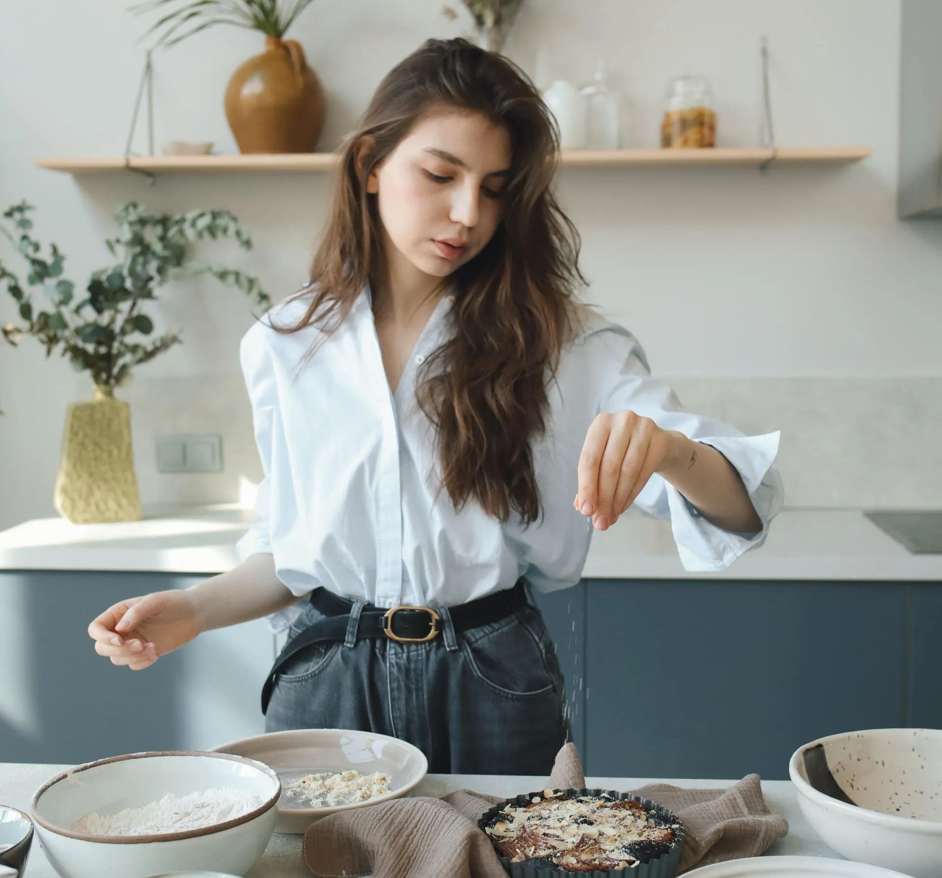 A woman in a white shirt is preparing food in a kitchen.