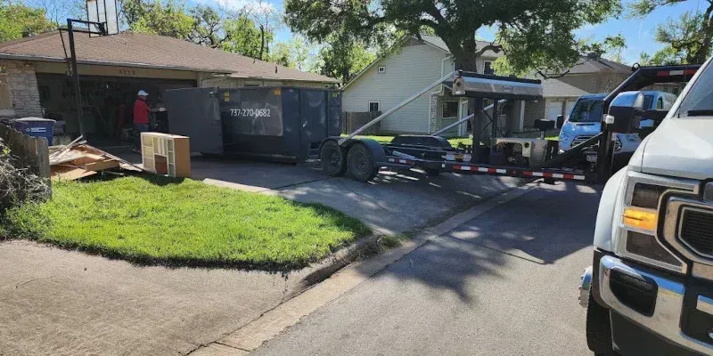 A utility trailer loaded with items covered by a plastic tarp is parked on a residential driveway near a house.