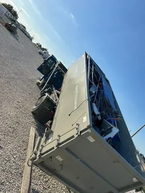 A large, gray industrial dumpster filled with scrap metal sits on a gravel lot under a clear blue sky.