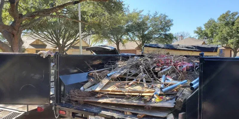 A dump truck filled with a heap of scrap metal, including twisted bicycle frames and wood, parked outdoors.