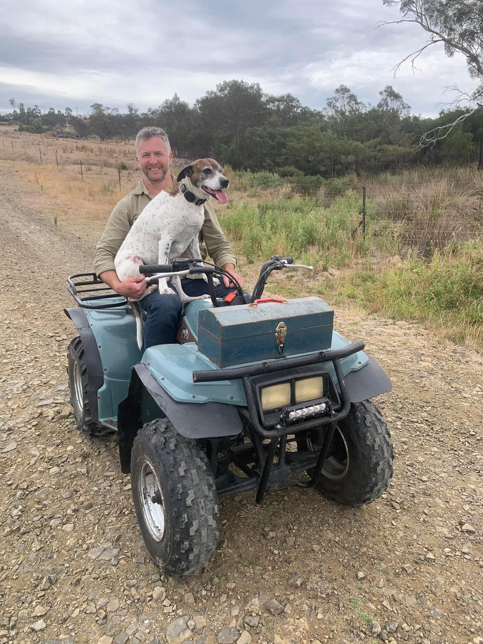 A man and a dog are riding a four wheeler on a dirt road.