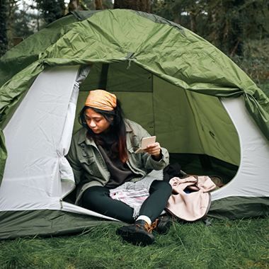 A woman is sitting in a tent looking at her phone.