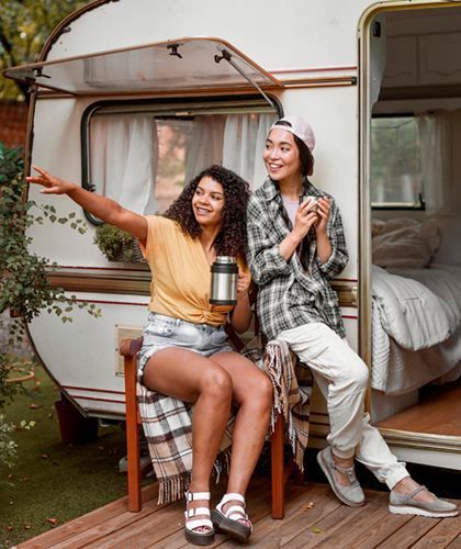 Two women are sitting on a bench in front of a trailer.