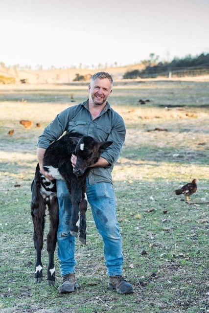 A man is holding a calf in his arms in a field.
